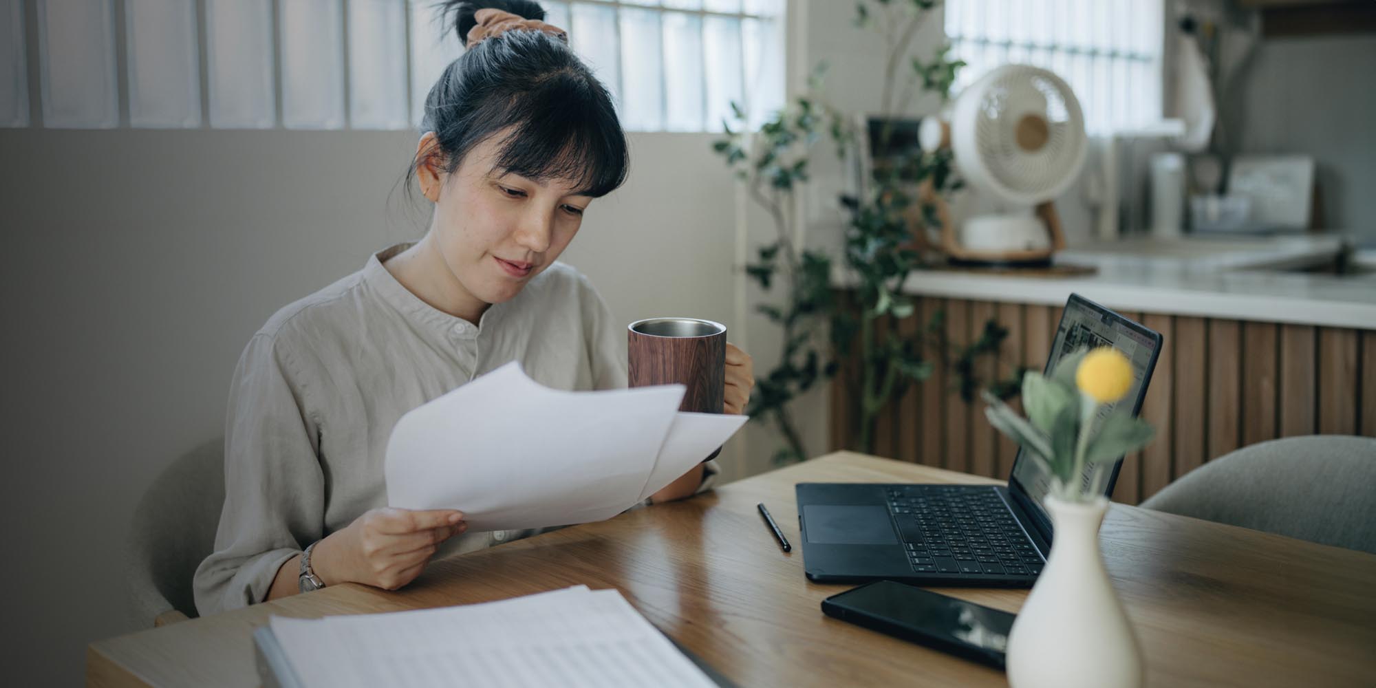 Woman looking at papers and computer while holding mug